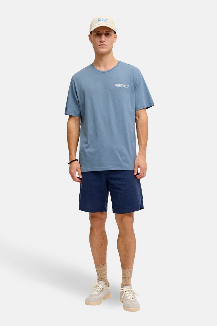 Blauw T-shirt met korte mouwen van JJREBEL, met tekstprint, gedragen met donkerblauwe shorts, beige sokken en sneakers.
