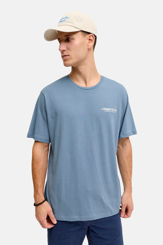 Blauw T-shirt met korte mouwen van JJREBEL, gedragen met een beige pet en een kralen armband.
