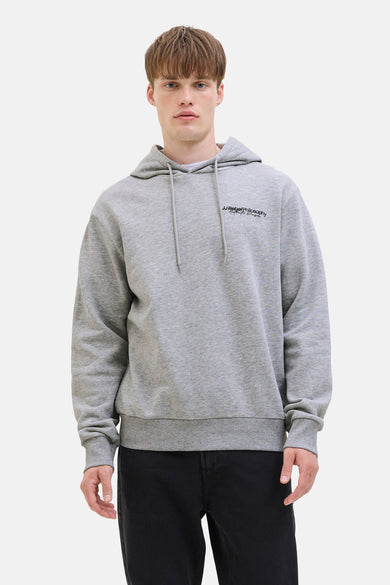 Pull-over gris avec capuche JJREBEL, avec un petit texte sur la poitrine, porté avec un jean noir.