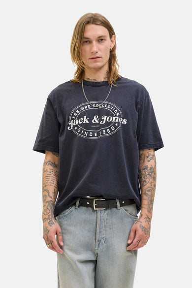 T-shirt noir à manches courtes d'ORIGINALS BY JACK & JONES, avec une impression blanche, porté avec des jeans larges et des baskets blanches.