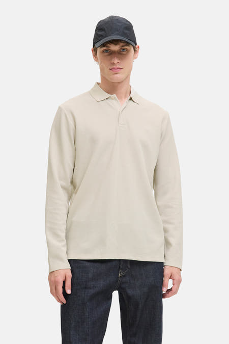 Pull beige à col V de PREMIUM BLUE par JACK & JONES, porté avec des jeans bleus foncés et un chapeau.