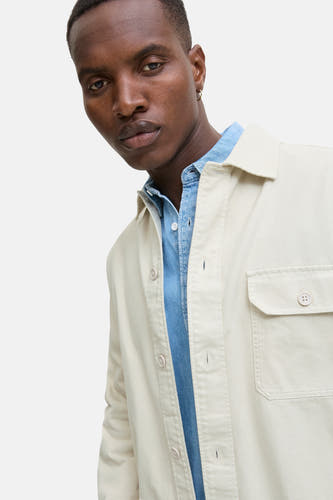 Beige overhemd van PREMIUM BLUE by JACK & JONES, met borstzak en knoopsluiting, gedragen over een blauw denim overhemd.