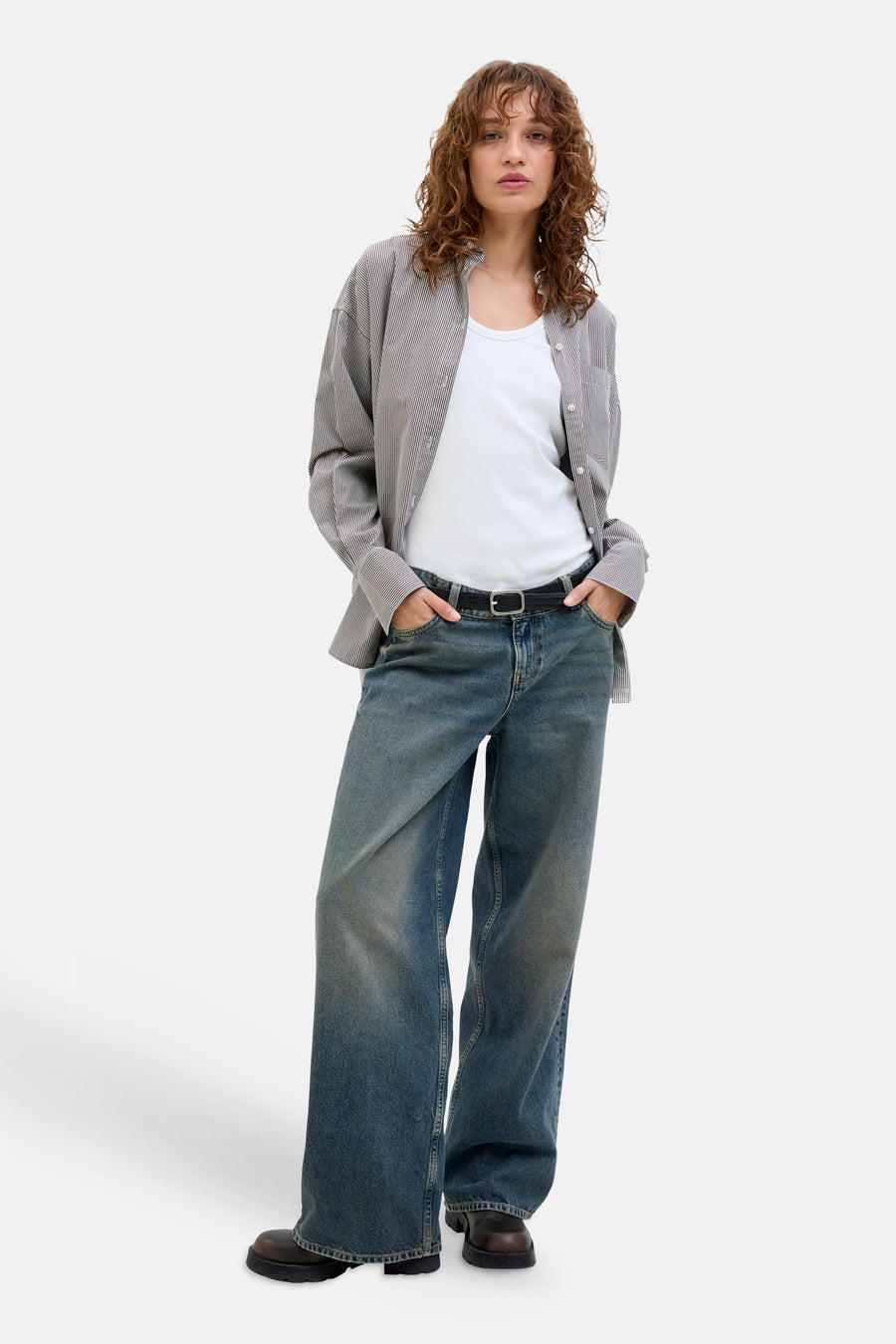 Witte tanktop van JJXX gedragen door een model met een open gestreept overhemd, wijde jeans en bruine laarzen.