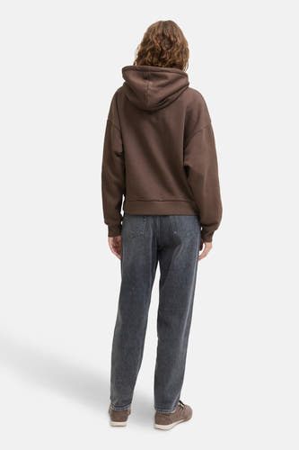 Pull-over marron avec capuche JJXX, à une coupe décontractée, associé à un jeans foncé et des baskets marrons.