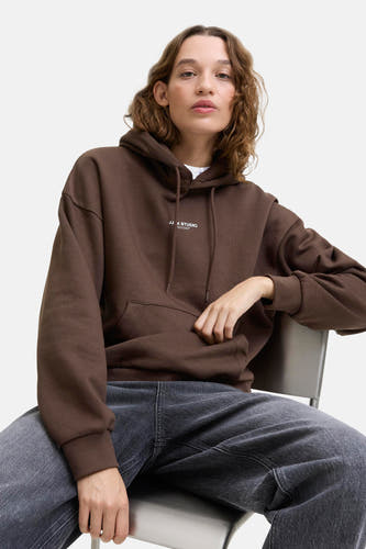 Pull-over marron avec capuche JJXX, modèle assis avec un sac à dos et des jeans foncés.