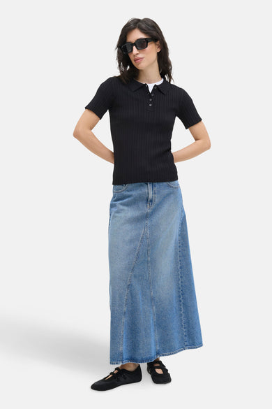 Pull noir JJXX, à manches courtes et col polo, associé à une jupe denim longue et des chaussures noires.