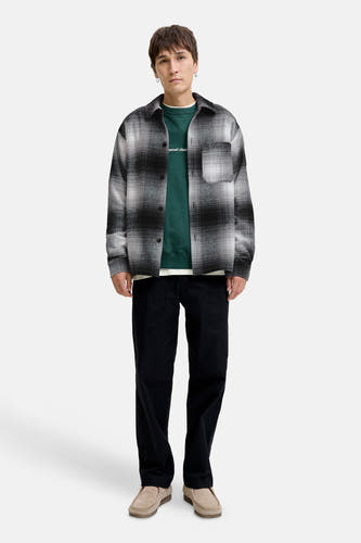 Chemise noire à manches longues de CORE BY JACK & JONES, avec un motif à carreaux noir et blanc, portée avec une veste verte et un pantalon noir.