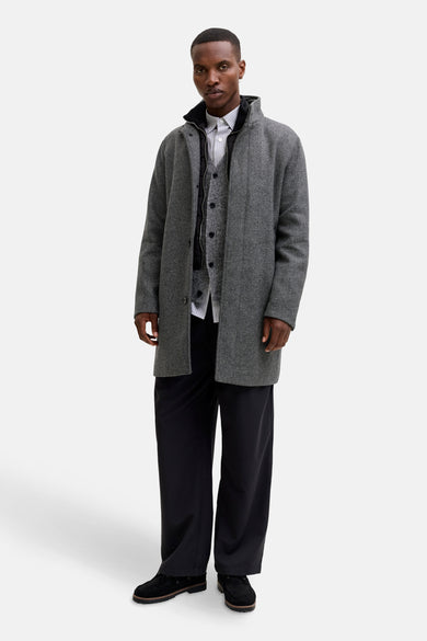 Lange grijze jas van PREMIUM by JACK & JONES, met een visgraatmotief en gedragen over een vest en broek.
