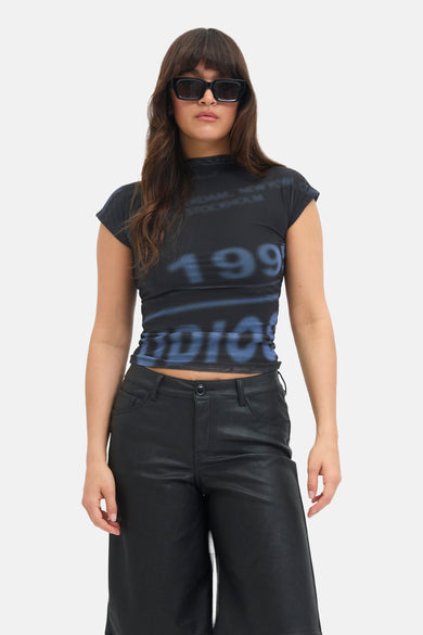 Blauw T-shirt met korte mouwen van JJXX, met bedrukte cijfers en model draagt een zwarte broek en zonnebril.
