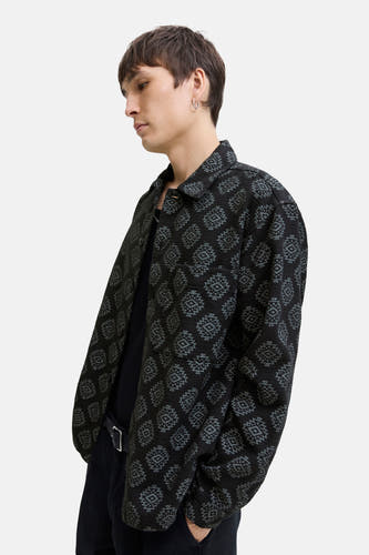 Chemise noire à manches longues de CORE BY JACK & JONES, avec un motif graphique, portée avec un pantalon noir et une ceinture.