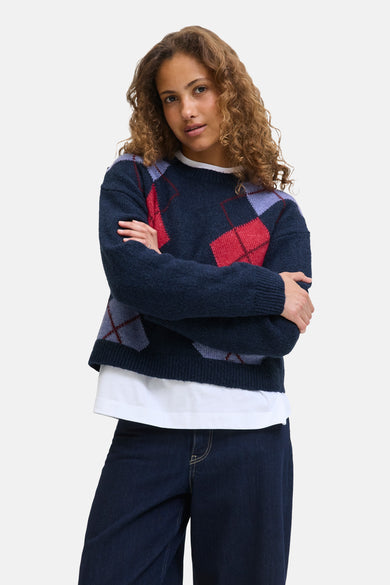T-shirt bleu avec col rond de JJXX, à carreaux d'argyle et associé à une chemise blanche et des jeans foncés.