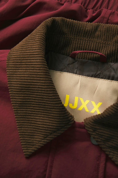 Rode jas van JJXX, met bruine ribfluwelen kraag en geborduurde logo op de achterkant.
