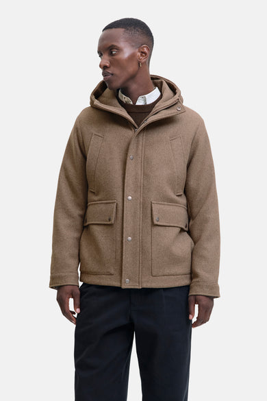 Beige lange jas van PREMIUM by JACK & JONES, met capuchon en zakken, gedragen met een overhemd en trui.
