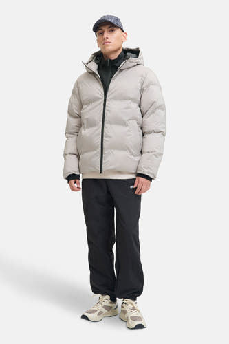 Korte ecru jas van CORE BY JACK & JONES, met capuchon en zwarte ritssluiting, gecombineerd met zwarte trainingsbroek en beige sneakers.