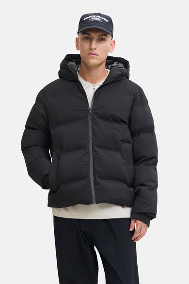Zwarte korte jas van CORE BY JACK & JONES, met capuchon en een model met een hand in de zak.
