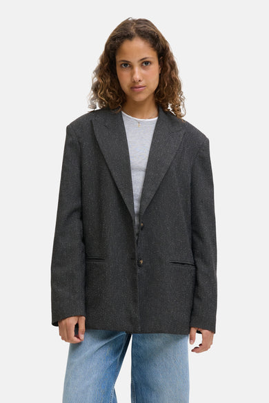 Blazer gris de JJXX, avec des détails subtils et porté sur un t-shirt gris et des jeans bleus.