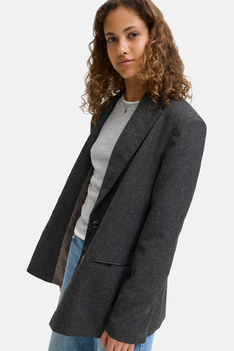Grijze blazer van JJXX met een getextureerde afwerking, gecombineerd met een grijs shirt en blauwe jeans.
