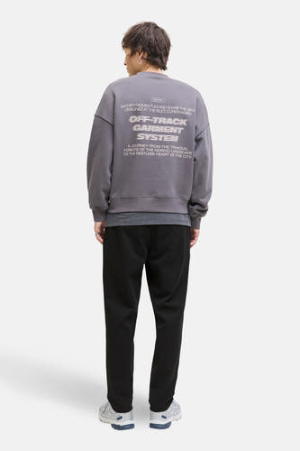 Zwarte broek van JACK & JONES JEANS INTELLIGENCE, gecombineerd met een grijze sweater met print op de rug en sneakers.