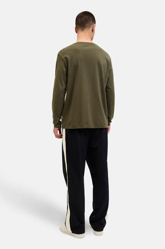 Gilet de kaki de CORE BY JACK & JONES, avec des manches longues, porté avec un pantalon de jogging noir à des rayures blanches.