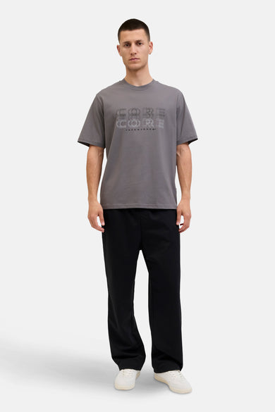 Grijs T-shirt met korte mouwen van CORE by JACK & JONES, met grafische print op de borst, gecombineerd met zwarte broek en witte schoenen.