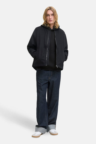 Pull-over noir avec capuche de CORE BY JACK & JONES, porté avec un manteau noir et des jeans larges bleu marine.