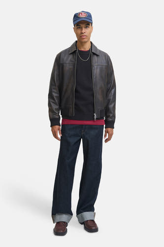 Zwarte trui met ronde hals van ORIGINALS BY JACK & JONES, gedragen onder een leren jack, met een spijkerbroek en bruine schoenen.