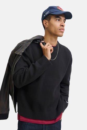 Pull noir à col rond de ORIGINALS BY JACK & JONES, avec une veste en cuir sur l'épaule et une chaîne argentée.