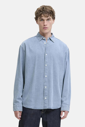 Lichtblauw spijkeroverhemd met lange mouwen van ORIGINALS BY JACK & JONES, met witte knopen, ruime pasvorm, gedragen op een donkere jeans.