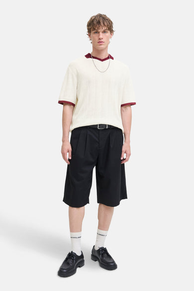 Ecru polo met korte mouwen van ORIGINALS BY JACK & JONES, afgewerkt met rode details, gedragen met zwarte shorts, witte sokken en zwarte schoenen.
