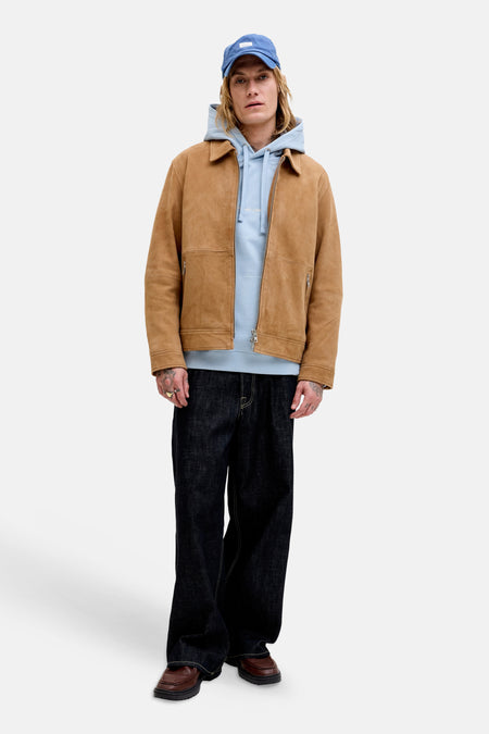 Blauwe hoodie van ORIGINALS by JACK & JONES, gedragen door een man met een blauwe pet, bruine suède jas en donkere jeans.