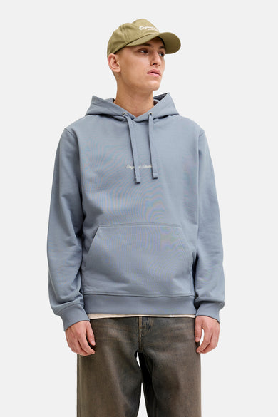 Sweat à capuche bleu de ORIGINALS BY JACK & JONES, porté avec une veste en cuir, un pantalon ample et une casquette.