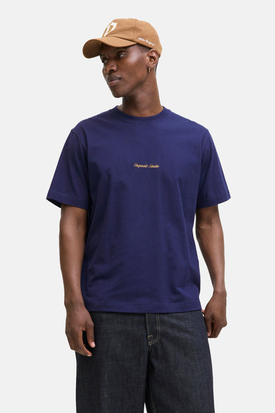 T-shirt bleu à manches courtes d'ORIGINALS BY JACK & JONES, avec du texte brodé, porté avec un chapeau marron et des jeans foncés.