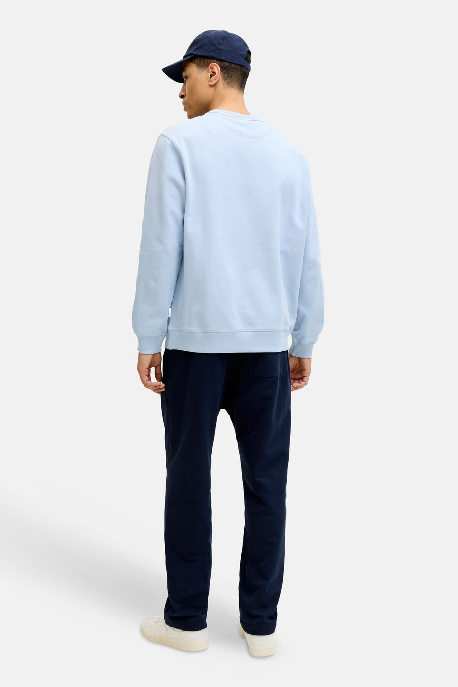 Lichtblauwe sweater met ronde hals van ORIGINALS BY JACK & JONES, met geribde boorden en zoom, achterkant zichtbaar op een man met donkerblauwe joggingbroek en pet.