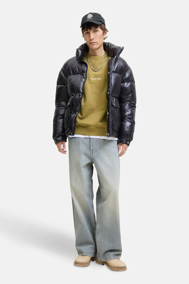 Groene sweater van ORIGINALS BY JACK & JONES, met een witte opdruk en gecombineerd met een zwarte pufferjas en wijde jeans.
