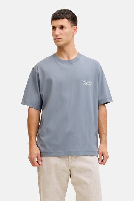 Blauw T-shirt met korte mouwen van ORIGINALS BY JACK & JONES, met witte letters op de borst, gedragen met een beige broek.
