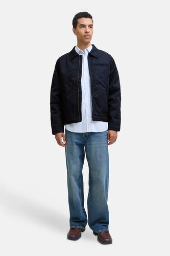 Blauwe korte jas van ORIGINALS BY JACK & JONES, gedragen over een lichtblauw overhemd met wijdvallende jeans en bruine schoenen.
