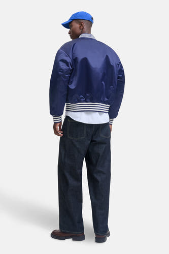 Blauwe jas van ORIGINALS BY JACK & JONES, met gestreepte boorden, gedragen met een gestreept overhemd en donkere jeans.
