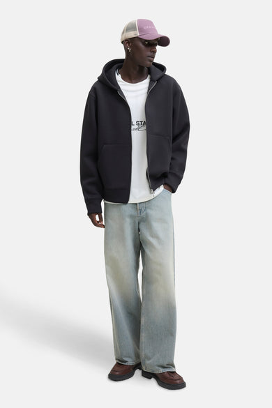 Gilet noir CORE BY JACK & JONES, porté sur un chemise blanc, avec des jeans bleus délavés et des chaussures brunes, avec une casquette violette.