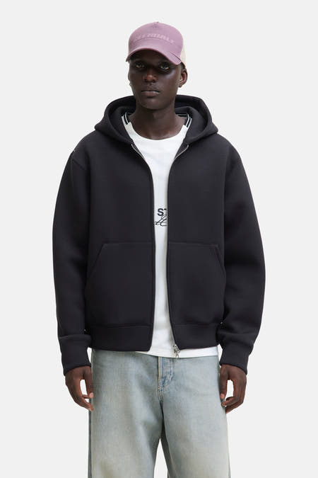 Pull-over noir de CORE BY JACK & JONES, avec fermeture à glissière et capuche, porté sur un T-shirt blanc et des jeans bleu clair.