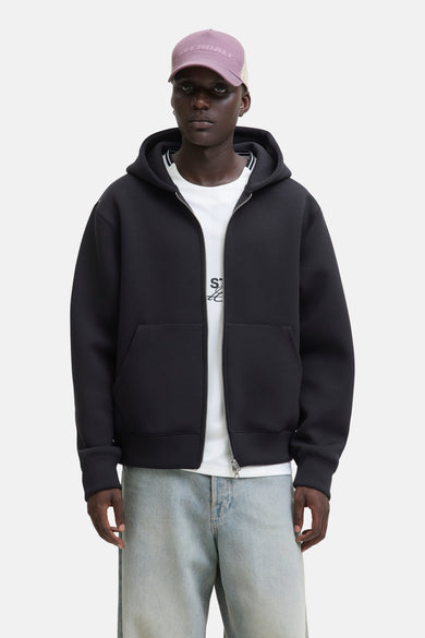 Pull-over noir de CORE BY JACK & JONES, avec fermeture à glissière et capuche, porté sur un T-shirt blanc et des jeans bleu clair.