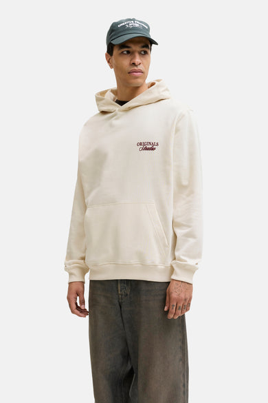 Pull à capuche beige de ORIGINALS BY JACK & JONES, à manches longues et coupe décontractée, porté sous une veste en cuir.