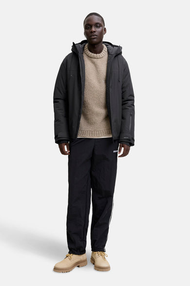 Zwarte korte jas van CORE BY JACK & JONES, met capuchon en gedragen met een trui en joggingbroek.
