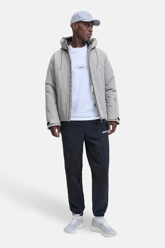 Grijze korte jas van CORE BY JACK & JONES, met capuchon en zwarte joggingbroek en grijze sneakers.
