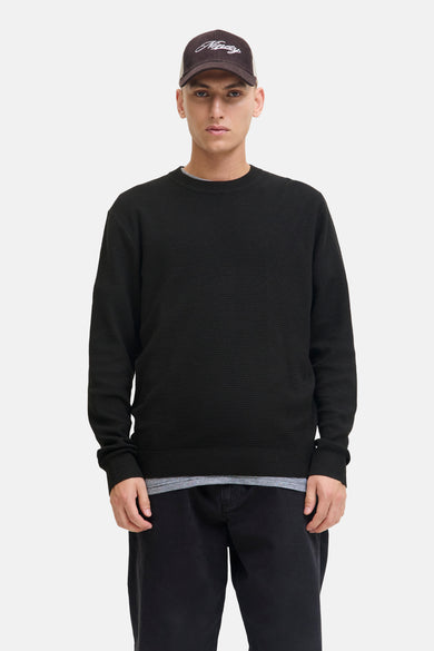 Zwarte trui met ronde hals van CORE BY JACK & JONES, gedragen met een baseball cap en een gestreept shirt.