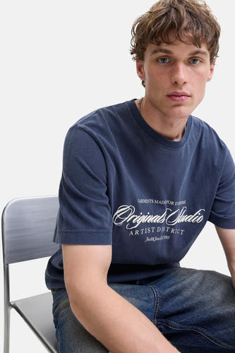T-shirt bleu à manches courtes d'ORIGINALS BY JACK & JONES, avec une impression de texte blanche et porté avec un jean bleu.