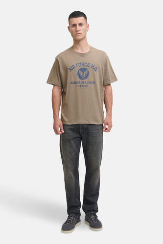 Kaki T-shirt met korte mouwen van PREMIUM BLUE by JACK & JONES, met blauwe tekst en logo, gecombineerd met donkere jeans en schoenen.
