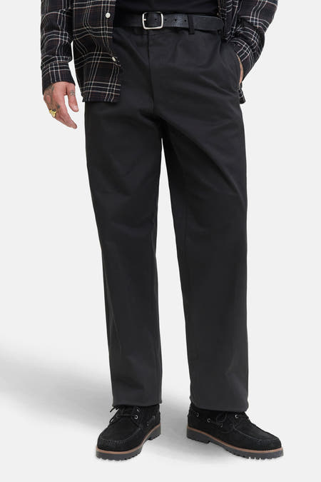 Jean noir chino de JACK & JONES JEANS INTELLIGENCE, porté avec une ceinture noire et des chaussures en cuir de mouton.