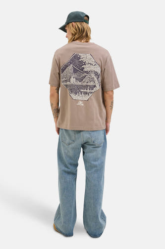 T-shirt marron à manches courtes d'ORIGINALS BY JACK & JONES, avec un imprimé sur le dos et associé à des jeans larges et une casquette.