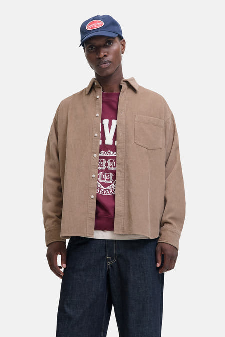 Bruin overhemd met lange mouwen van ORIGINALS BY JACK & JONES, met corduroy textuur, gedragen over een bordeauxrode sweater met print en donkerblauwe jeans.

