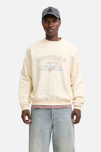 Beige sweater van ORIGINALS BY JACK & JONES, met vintage print op de borst, gecombineerd met blauwe jeans en een grijze pet.